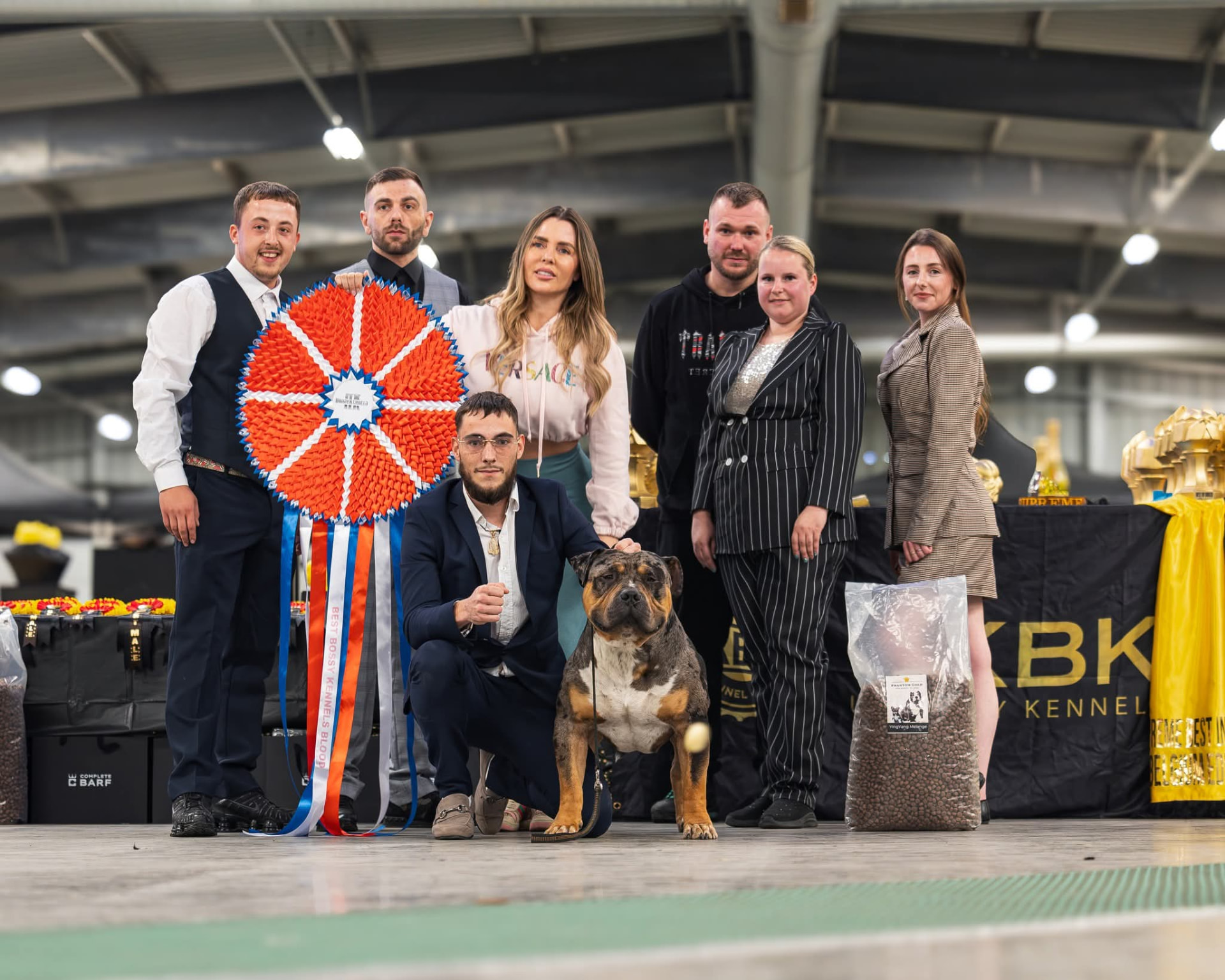 Winning team photographed in the ring with a large championship ribbon and their bully breed dog
