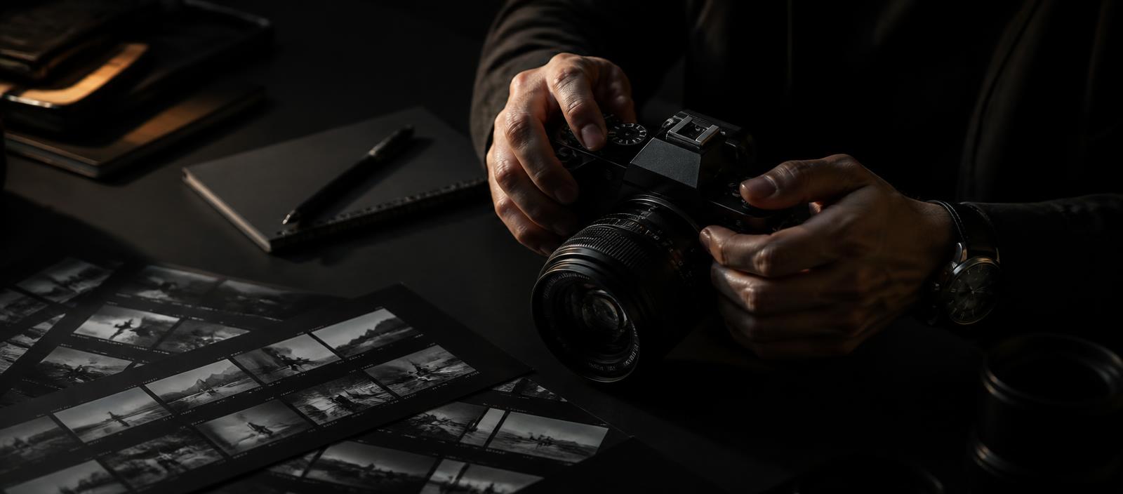 Photographer's hands holding a camera beside contact sheets in low light